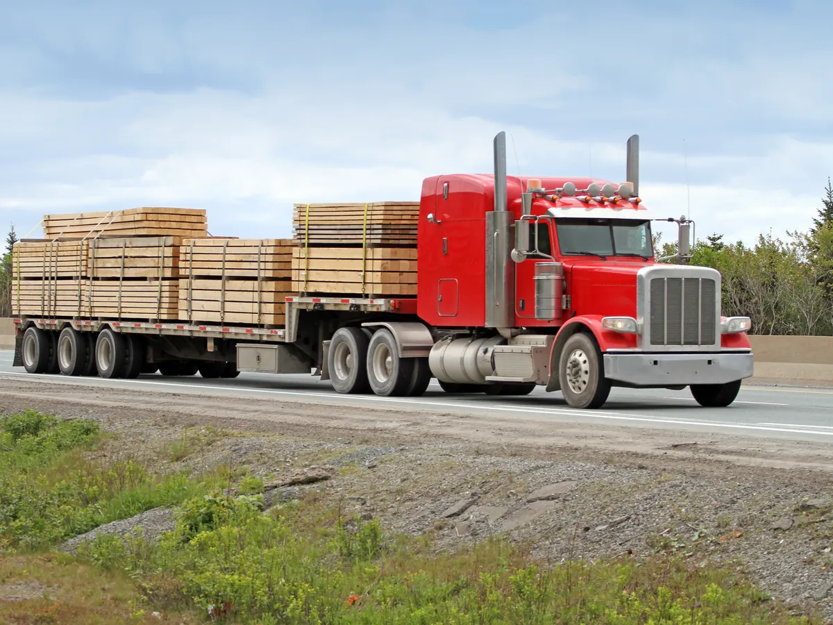 Loaded flatbed semi truck hauling strapped lumber on the highway — all-position versus trailer tire guide — Northwest Truck Tire Supply